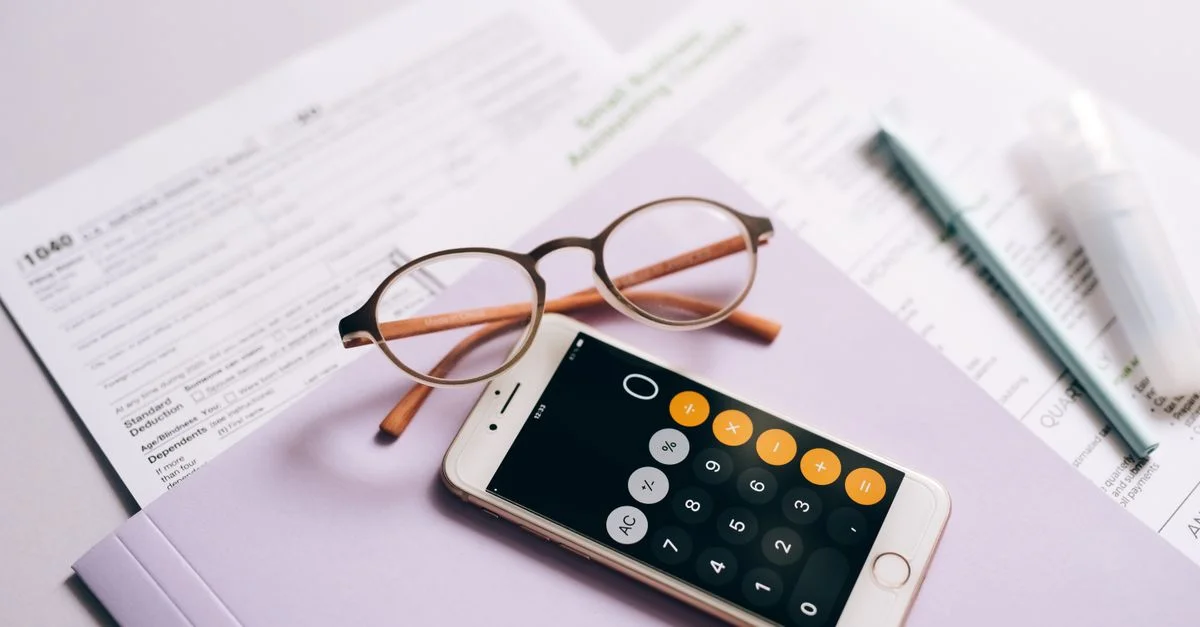 Une calculatrice de smartphone et des lunettes sur des documents fiscaux, représentant la préparation fiscale moderne.