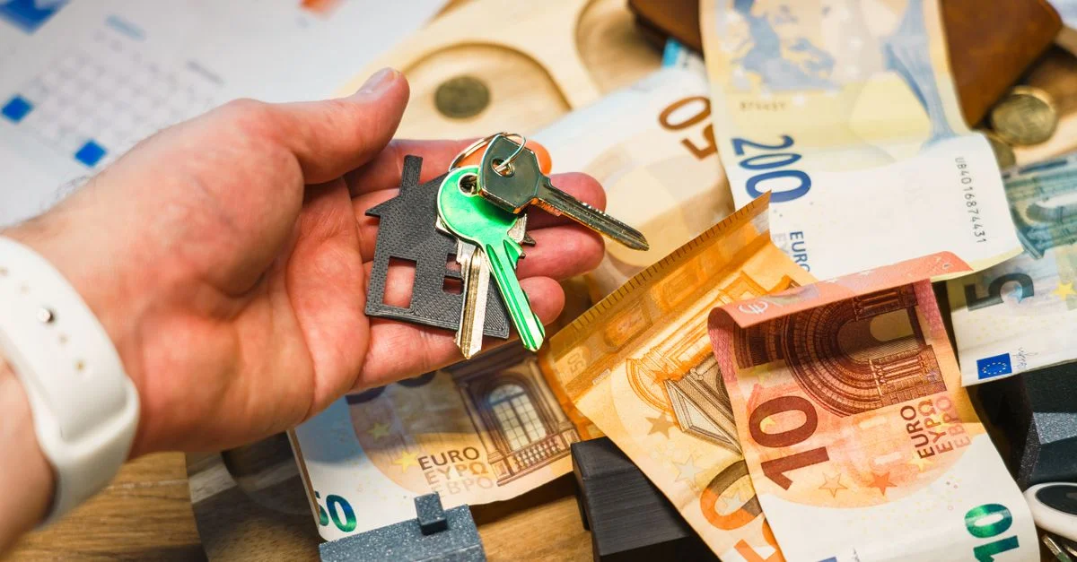 Une main tenant des clés de maison au-dessus de billets euro, symbolisant l'immobilier et la finance.