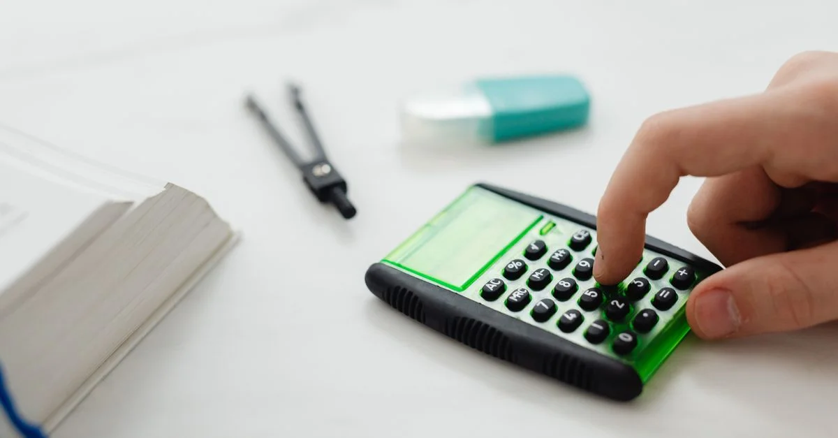 Gros plan sur la main d'une personne appuyant sur une calculatrice sur un bureau avec d'autres fournitures de papeterie.