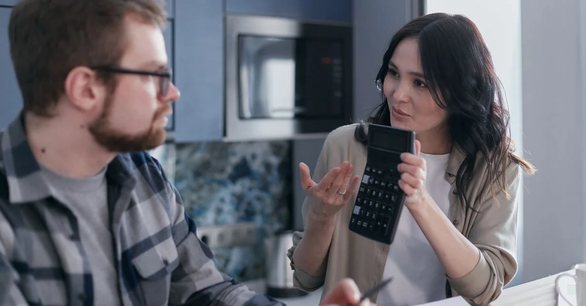 Un couple assis dans une cuisine discutant de questions financières en utilisant une calculatrice et des documents.