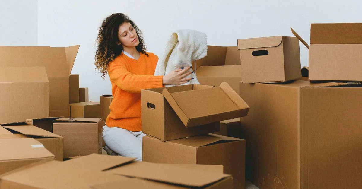 Une femme aux cheveux bouclés déballe des cartons dans son nouvel appartement. Jour du déménagement.