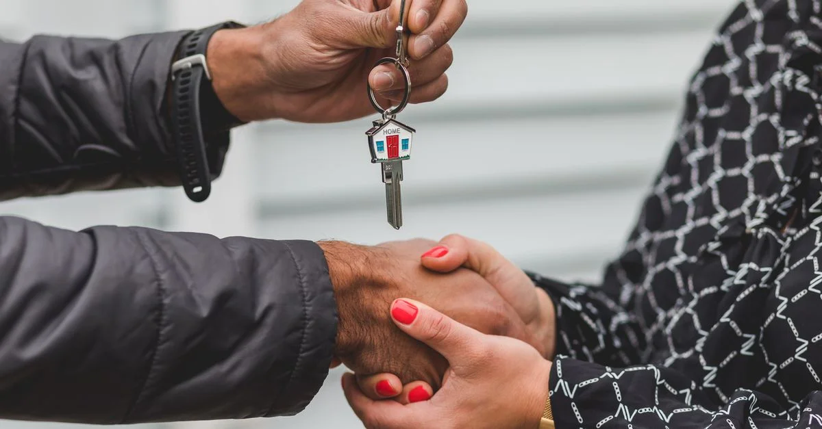 Gros plan d'un agent immobilier remettant une clé de maison à un nouveau propriétaire, symbolisant la possession et l'investissement.