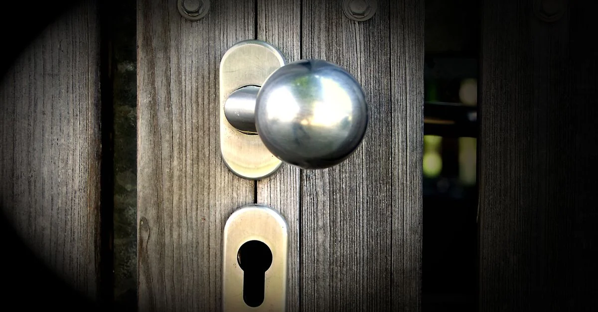 Vue en gros plan d'une poignée de porte en métal et d'un trou de serrure sur une porte en bois, mettant en avant la sécurité et le design.