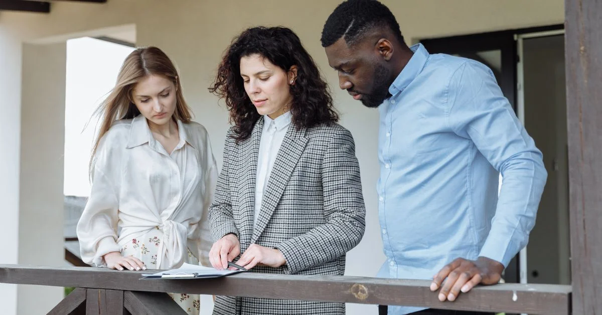 Trois adultes examinant des documents sur un balcon lors d'une consultation immobilière.