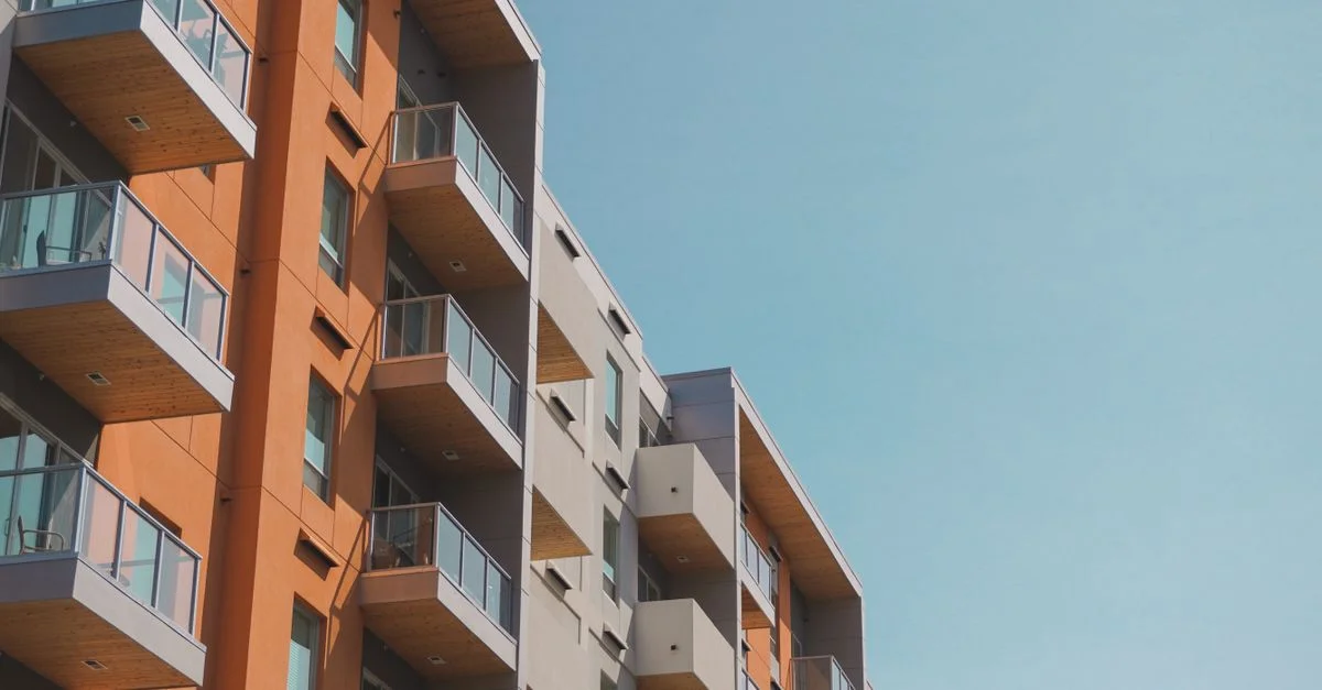 Immeuble contemporain avec balcons en verre sous un ciel bleu clair.