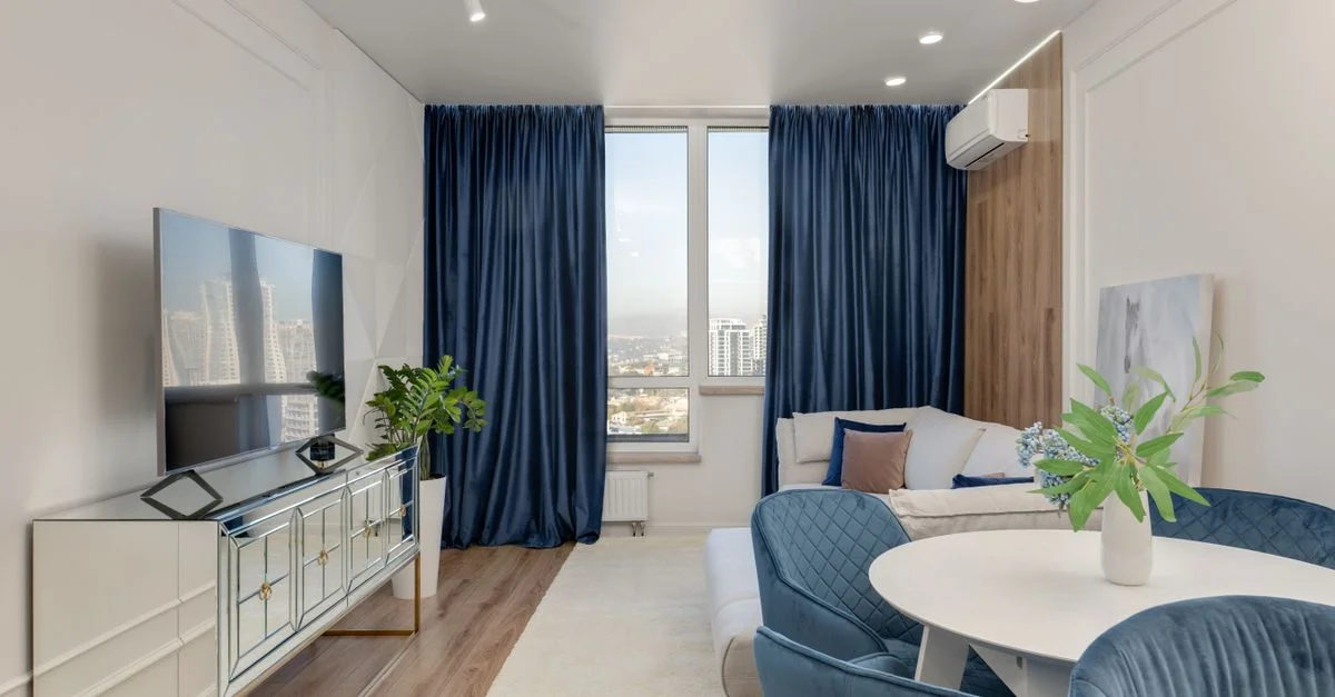 Salon élégant avec des rideaux en velours bleu, des meubles blancs et une vue sur la ville.